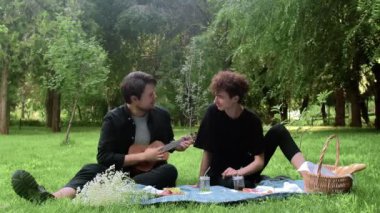 Bir adam yazın doğada başka bir adama ukulele çalıyor.