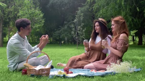 Un chico toma fotos de chicas en el teléfono en el verano en la naturaleza — Vídeos de Stock