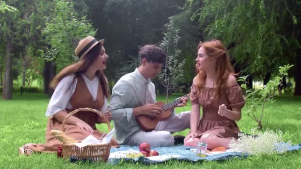 Un chico toca un ukelele, y las chicas cantan una canción en la naturaleza en el verano — Vídeos de Stock