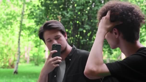 Un tipo toma fotos en el teléfono de otro tipo en la naturaleza en el verano — Vídeos de Stock
