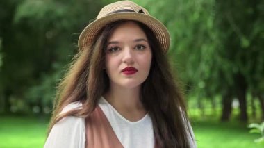 Şapkalı güzel bir kız gülümser ve yazın doğada kameraya bakar.