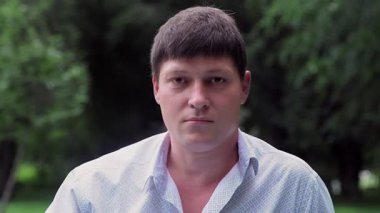 Ciddi bir adam yazın doğada kameraya bakar.