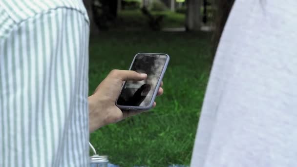 Een mensenhand houdt een telefoon vast en bladert in de zomer door foto 's in de natuur — Stockvideo