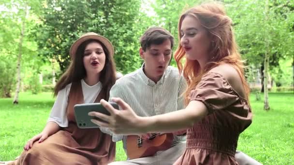 Flickan spelar in en video på sin telefon när hon och hennes vänner sjunger låtar i naturen på sommaren — Stockvideo