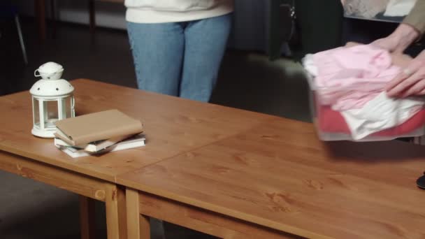 女性のクローズアップは、古着屋でテーブルの上に服を置いた箱を置く — ストック動画