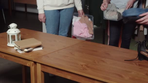 Kadınlar ikinci el giysi dükkanında kutuları ve elbiseleri masaya koyarlar. — Stok video