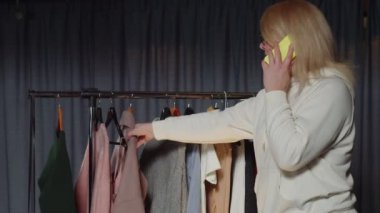 Genç kadın satıcı telefonla konuşuyor ve ikinci el giyim mağazasında çalışıyor.