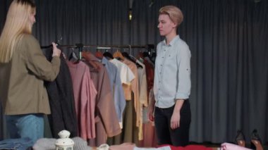 Genç bir kadın ikinci el giyim mağazasında siyah bir ceket deniyor.