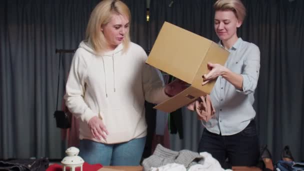 Femei tinere Lucrătorii de la magazin second hand sortează hainele pe masă — Videoclip de stoc