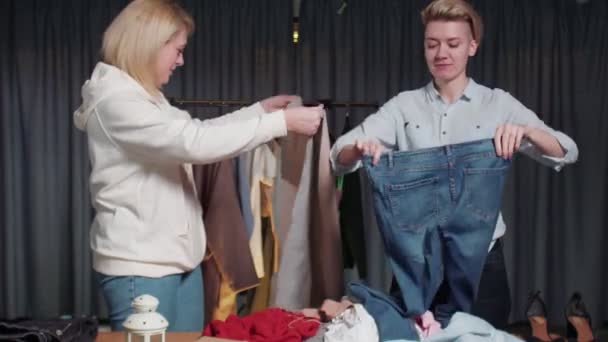 Junge Frauen aus dem Second-Hand-Laden sortieren Kleidung auf dem Tisch — Stockvideo