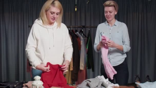 Mujeres jóvenes Trabajadoras de segunda mano clasifican la ropa en la mesa — Vídeo de stock