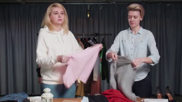 Молоді жінки Друга рука робітників магазину сортувати одяг на столі — стокове відео