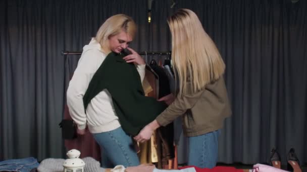 Блондинка примеряет зеленый свитер в магазине подержанной одежды — стоковое видео