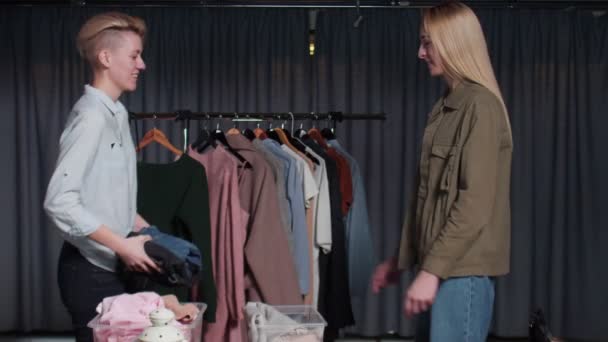 Detailní záběr jedné ženy prodejce dává oblečení jiné ženě zákazníka v second hand oblečení shop — Stock video