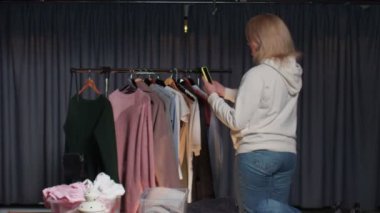 Sarışın kadın satıcı, ikinci el giysi dükkanındaki kıyafetlerin hikayelerini ya da videosunu kaydeder.