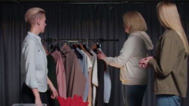 Sarışın kadın ikinci el giysi dükkanında siyah ceket deniyor.