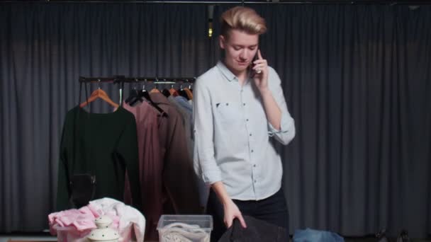 Vendedora joven habla por teléfono y trabaja en tienda de ropa de segunda mano — Vídeos de Stock