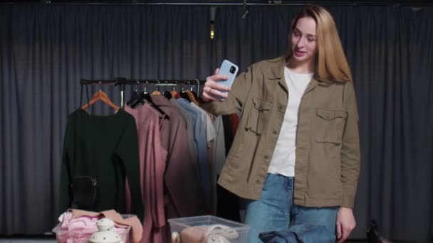 Joven vendedora registra historias de ropa en su teléfono en tienda de ropa de segunda mano — Vídeo de stock
