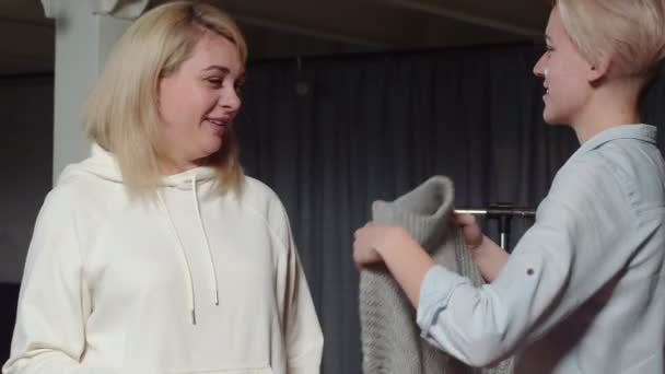 Kobieta próbuje na szarym swetrze w sklepie z używanymi ubraniami — Wideo stockowe