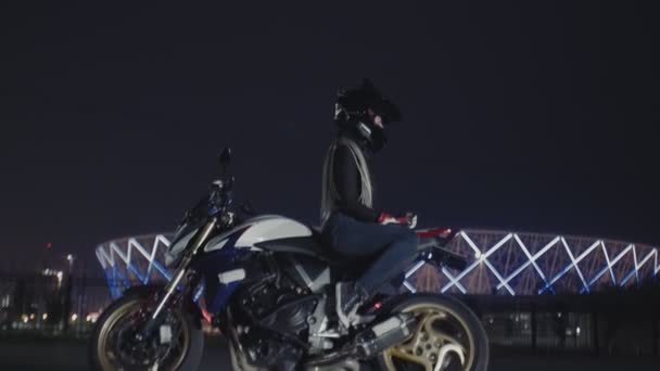 Schöne Frau mit schwarzem Helm sitzt auf einem Motorrad vor dem Hintergrund eines Stadions — Stockvideo