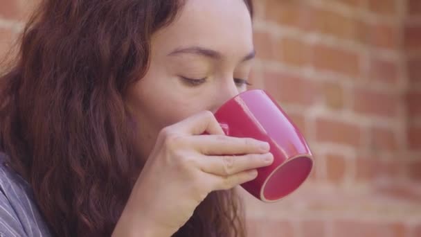 Egy gyönyörű göndör hajú lány teát iszik és élvezi az ízét az utcán. — Stock videók