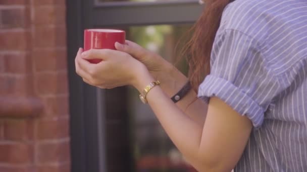 美しい巻き毛の女の子がお茶を飲み、通りでその味を楽しんでいます — ストック動画