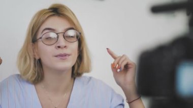 Kanepede oturan, gülümseyen ve kamerayla konuşan gözlüklü genç bir kadının yakın çekimi. Abonelerine veda ediyor.