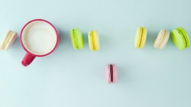 Çok renkli Fransız makarnası kurabiyeleri ve pastel mavi arka planda bir fincan kahve.