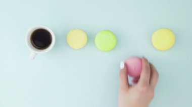 Çok renkli Fransız makarnası kurabiyeleri ve pastel mavi arka planda bir fincan kahve.