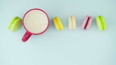 Çok renkli Fransız makarnası kurabiyeleri ve pastel mavi arka planda bir fincan kahve.