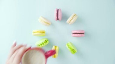 Çok renkli Fransız makarnası kurabiyeleri ve pastel mavi arka planda bir fincan kahve.