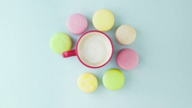 Çok renkli Fransız makarnası kurabiyeleri ve pastel mavi arka planda bir fincan kahve.