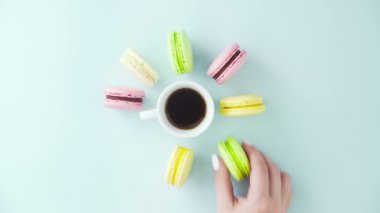 Çok renkli Fransız makarnası kurabiyeleri ve pastel mavi arka planda bir fincan kahve.