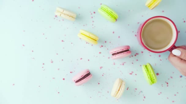 Vue de dessus de biscuits colorés, macarons français, et une tasse de café sur un fond bleu pastel avec des confettis magnifiquement dispersés — Video