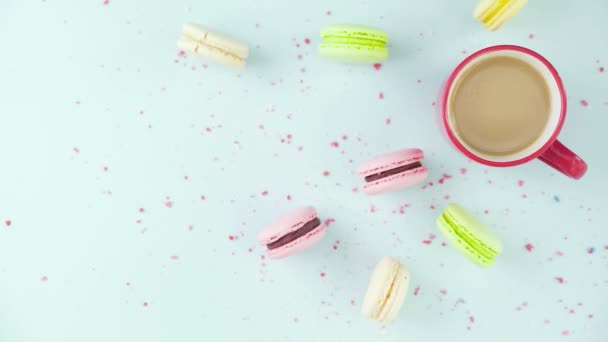 Vue de dessus de biscuits colorés, macarons français, et une tasse de café sur un fond bleu pastel avec des confettis magnifiquement dispersés — Video