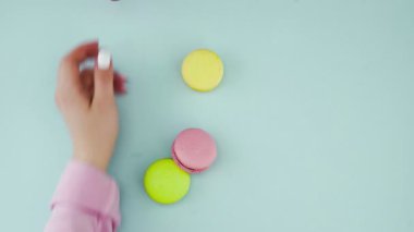 Çok renkli Fransız makarnası kurabiyeleri ve pastel mavi arka planda bir fincan kahve.
