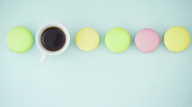 Çok renkli Fransız makarnası kurabiyeleri ve pastel mavi arka planda bir fincan kahve.