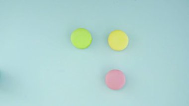 Çok renkli Fransız makarnası kurabiyeleri ve pastel mavi arka planda bir fincan kahve.