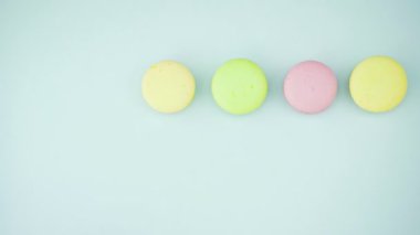 Çok renkli Fransız makarnası kurabiyeleri ve pastel mavi arka planda bir fincan kahve.
