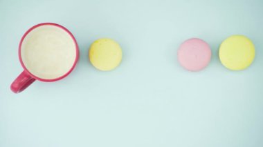 Çok renkli Fransız makarnası kurabiyeleri ve pastel mavi arka planda bir fincan kahve.