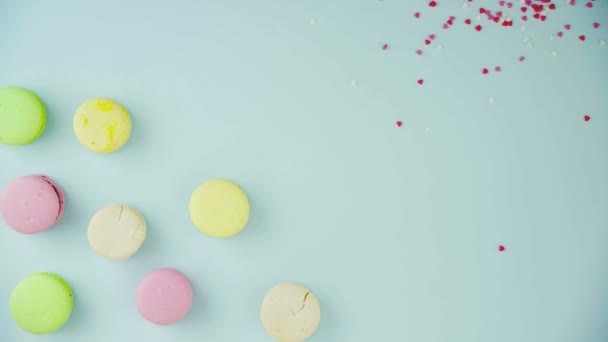 Ovanifrån av flerfärgade kakor Franska makaroner på en pastellblå bakgrund med vackert spridda konfetti — Stockvideo