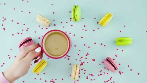 Renkli kurabiyeler, Fransız makarnaları ve pastel mavisi arka planda güzel dağınık konfetiyle bir fincan kahve. — Stok video