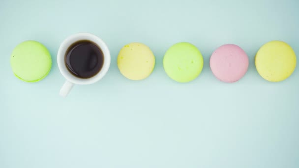 Widok z góry wielobarwne francuskie ciasteczka makaronowe i filiżankę kawy na pastelowym niebieskim tle — Wideo stockowe