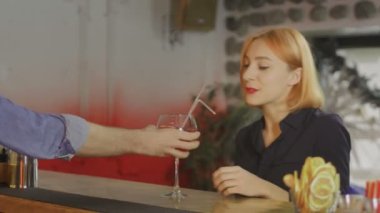 Bir kız elinde bir bardak şarapla barda oturuyor ve barmenle iletişim kuruyor.
