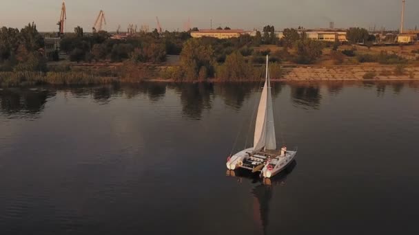 Küçük bir yelkenli yat gün batımında nehirde yelken açar. — Stok video