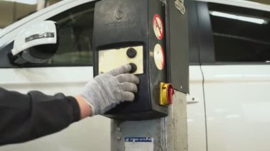 Araba tamircisi krikonun kaldırma ve taşıma mekanizmasındaki tuşa basarak arabayı indiriyor. Otomatik onarım, onarım, bakım