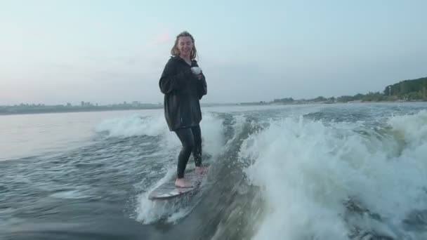 Surfařka skočí na wakeboard a vypije kávu nebo čaj z hrnku. Zkušený wakeboarder rozstřikuje do kamery kapky vody. — Stock video