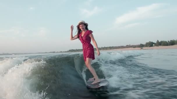 A female surfer in a red dress and hat jumps on a wakeboard. An experienced wakeboarder sprays water drops into the camera. — Stock Video