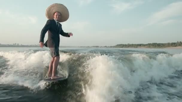 Surfař skákající na wakeboardu v obleku se slamákem na hlavě. Zkušený wakeboarder rozstřikuje do kamery kapky vody. — Stock video