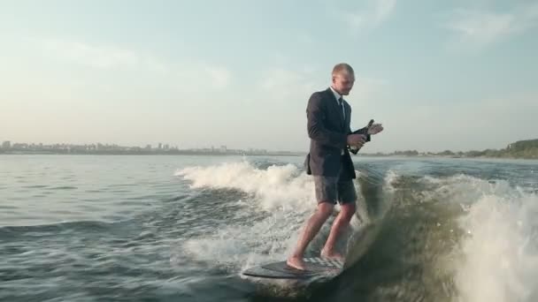 Egy boldog szörfös ugrál egy wakeboardon öltönyben egy üveg pezsgővel. Egy tapasztalt wakeboarder vizet permetez a kamerába.. — Stock videók